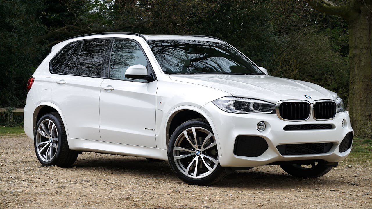 White BMW luxury SUV parked outdoors surrounded by trees in the UK.